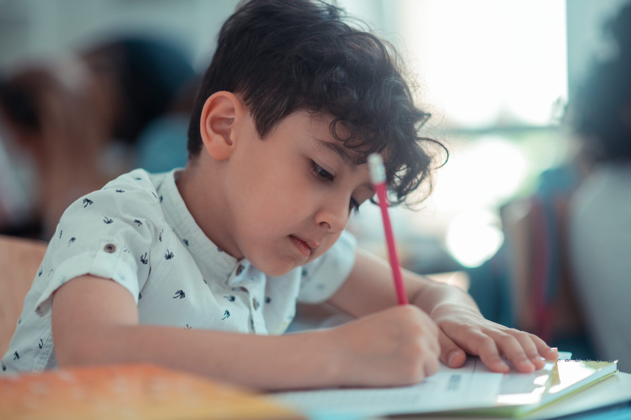Doing best. Concentrated school boy writing his test with the pencil during the lesson.