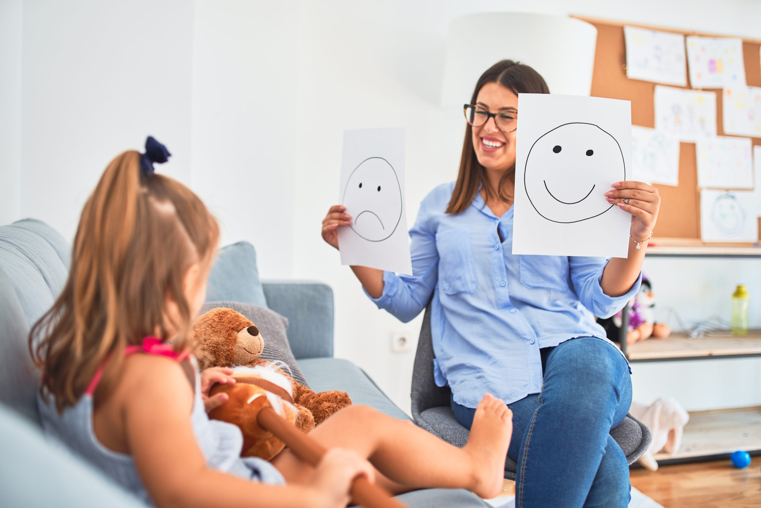 Young therapist woman speaking and treating child, counselor and behaviour correction at pedagogue payroom showing happy and sad faces